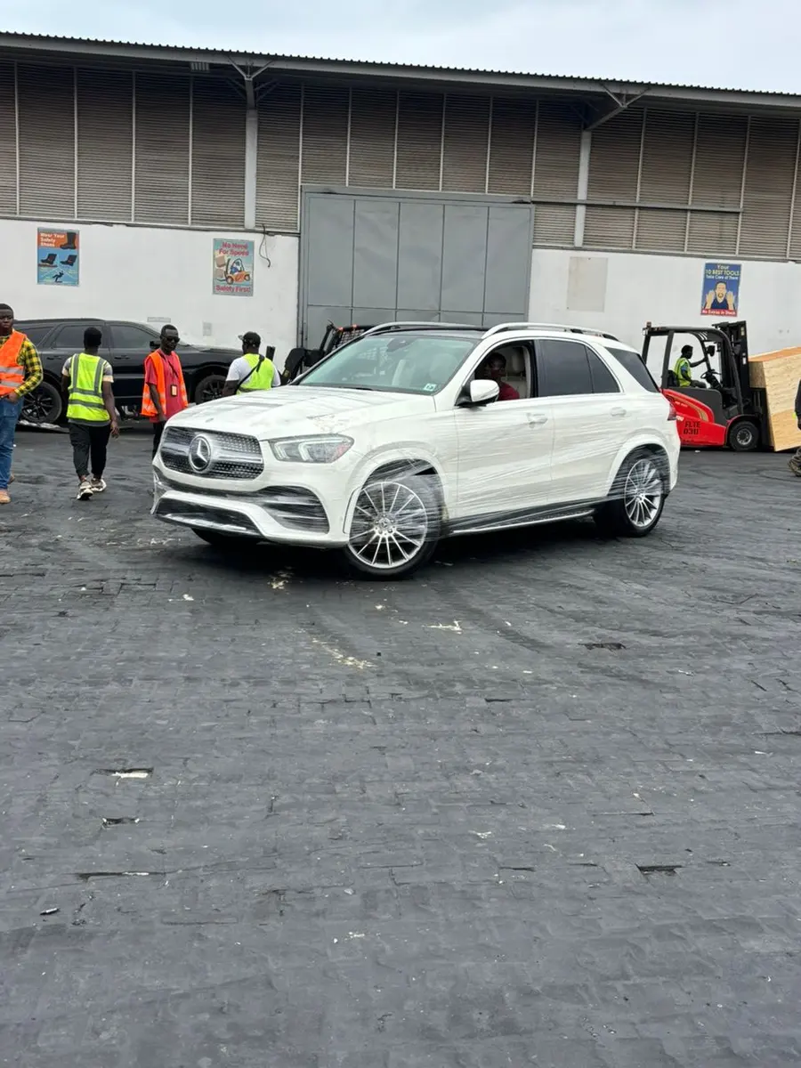 A white Mercedes SUV in a warehouse yard with a forklift and team
